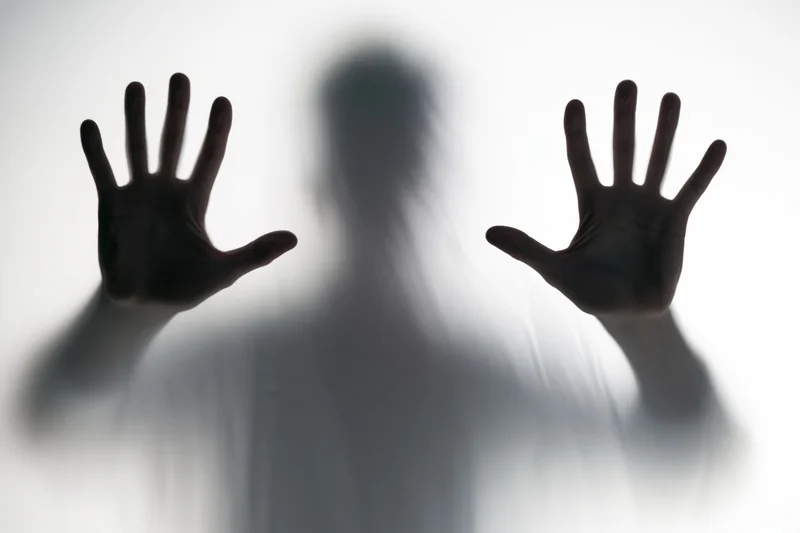 Silhouette of a person pressing hands flat against frosted glass