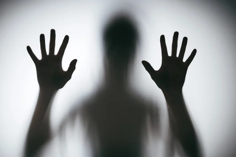 Silhouette of a person pressing hands flat against frosted glass