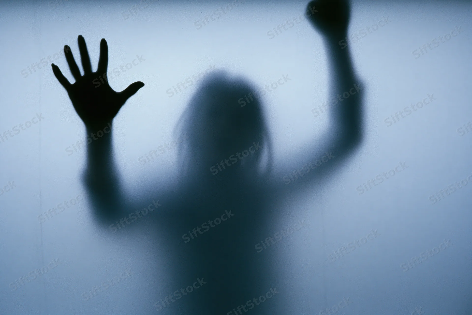 Silhouette of a woman pressing one hand flat against frosted glass with the other raised, indoors at night