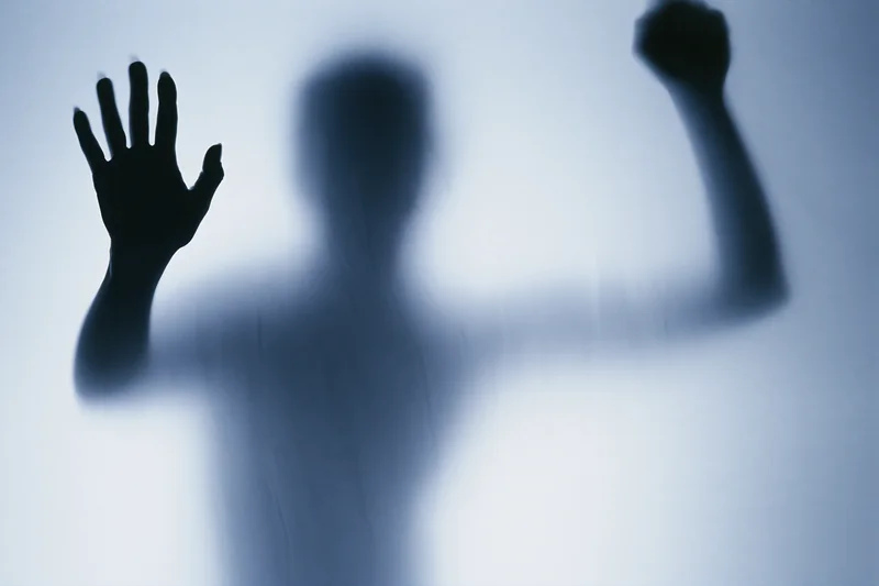 Silhouette of a woman pressing one hand flat against frosted glass with the other raised in a fist