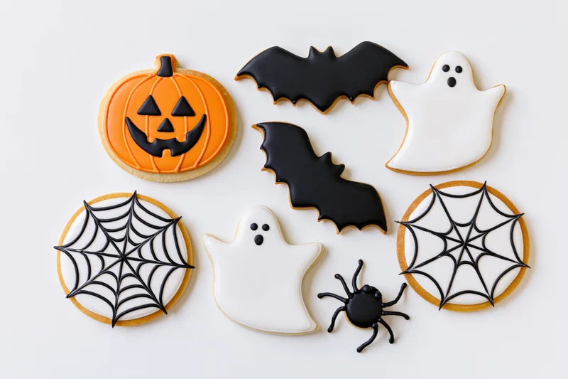 Halloween-themed sugar cookies decorated as pumpkins, ghosts, bats, and spiderwebs arranged flat on white surface