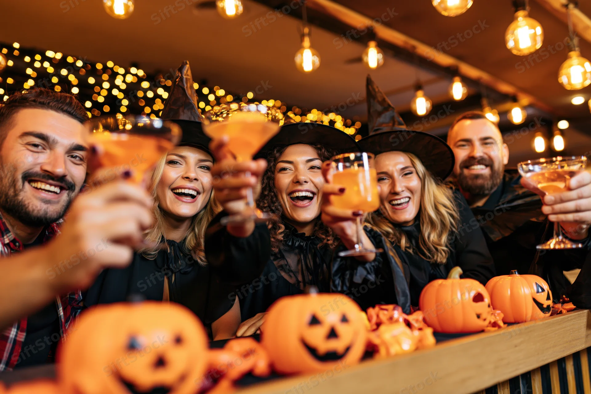 Six friends in witch costumes toasting with cocktails at a halloween bar party