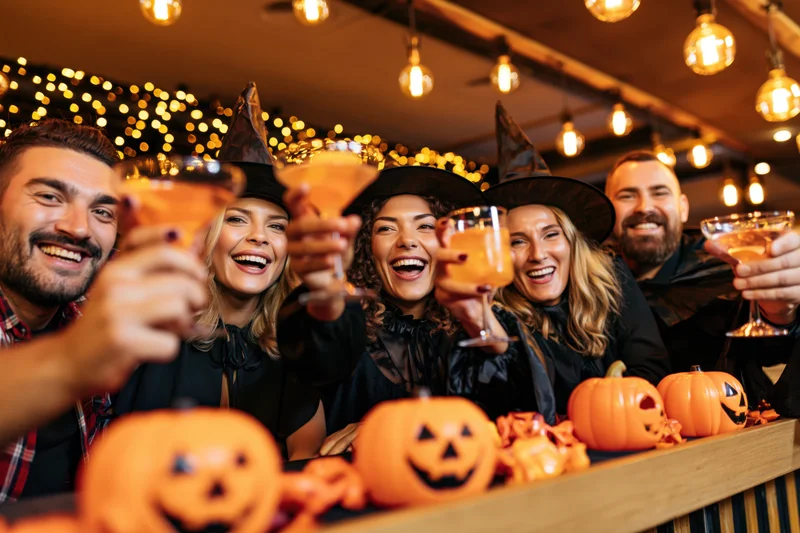 Six friends in witch costumes toasting with cocktails at a halloween bar party