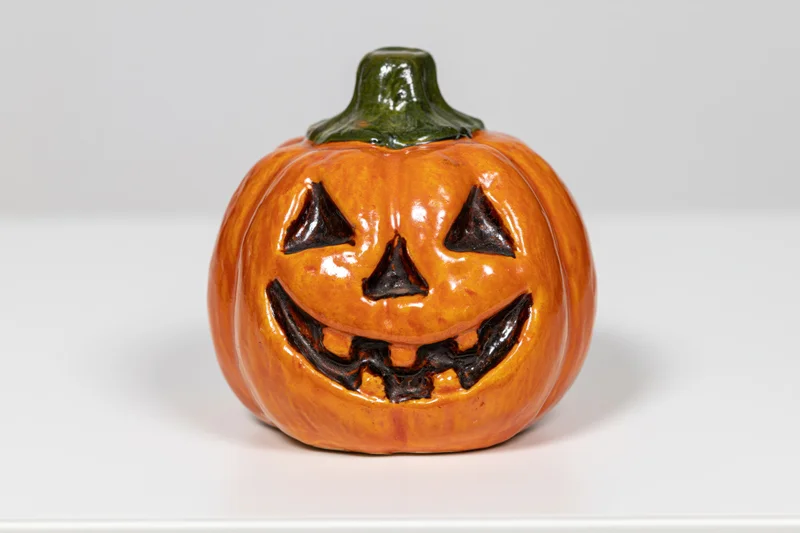 Ceramic jack-o-lantern figurine with carved smiling face on white surface