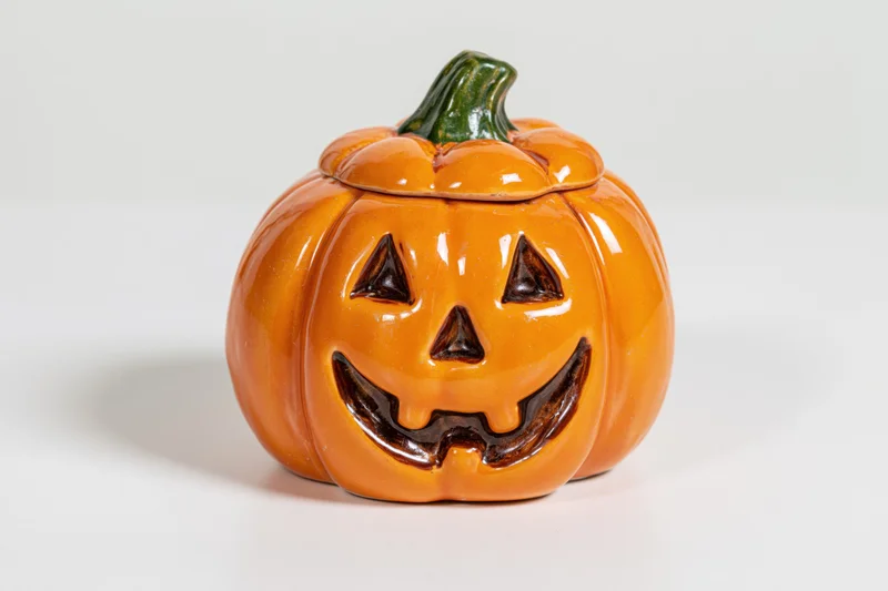 Ceramic jack-o-lantern figurine with carved smiling face and green stem on white background