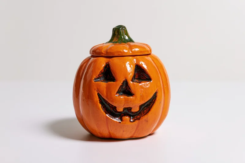 Ceramic jack-o-lantern figurine with carved smiling face and lid on white surface