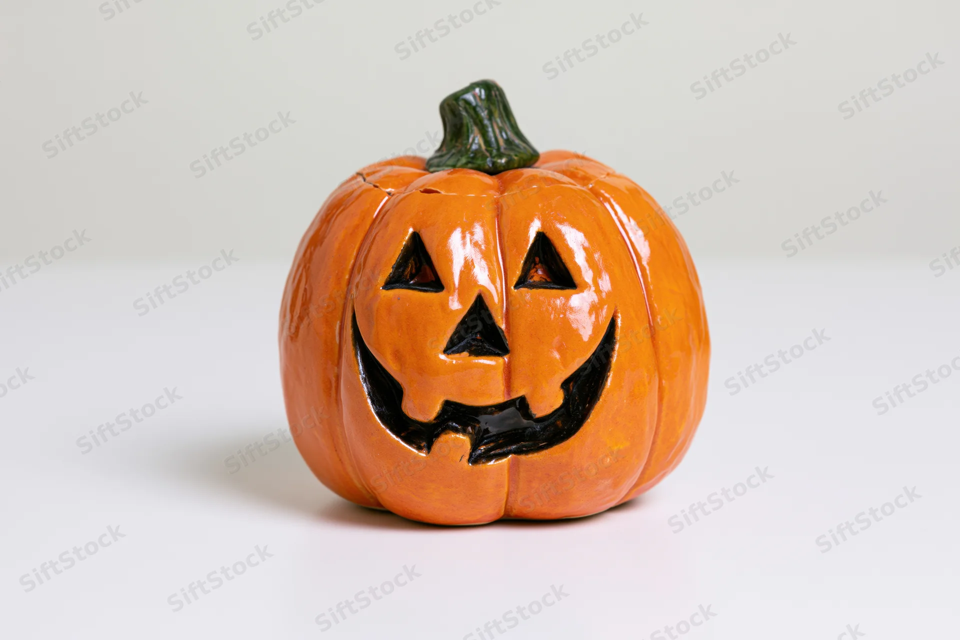 Small ceramic jack-o-lantern figurine with carved smiling face on white surface