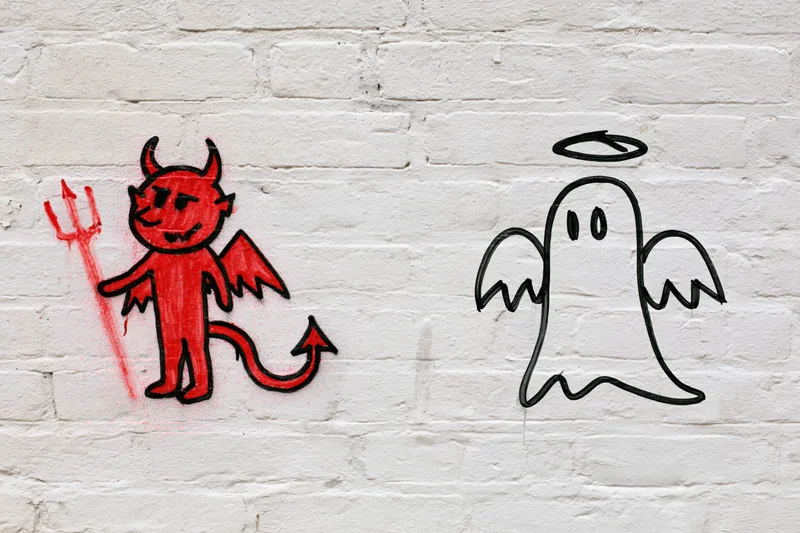 Red devil and white angel graffiti on a white brick wall