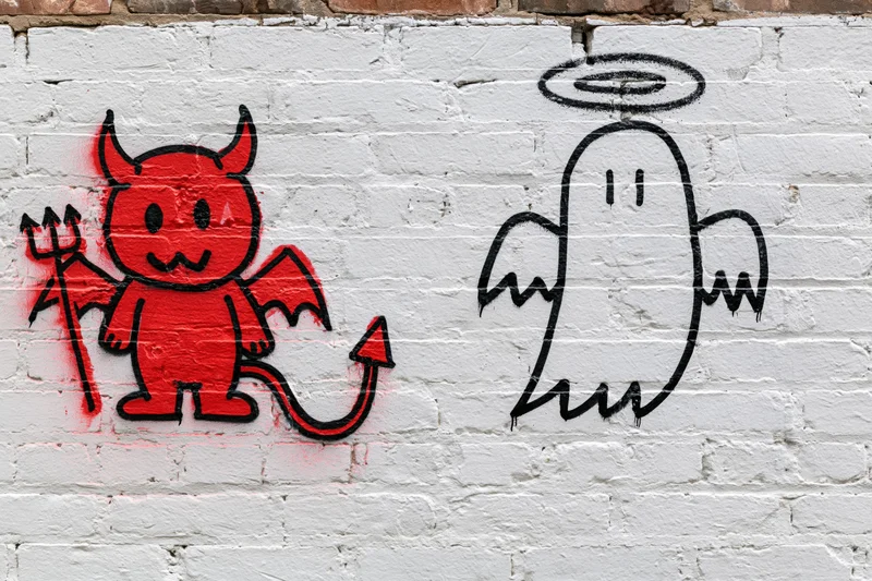 Red devil and black angel graffiti characters on white brick wall