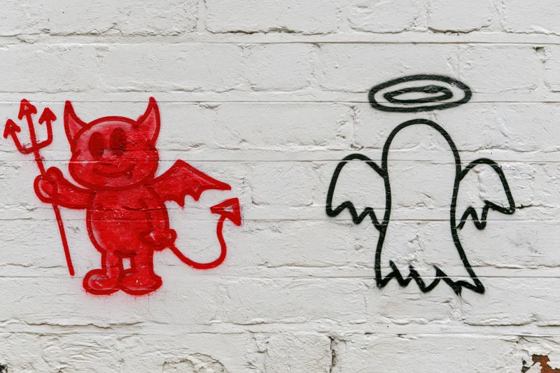Red devil and black angel graffiti on white brick wall