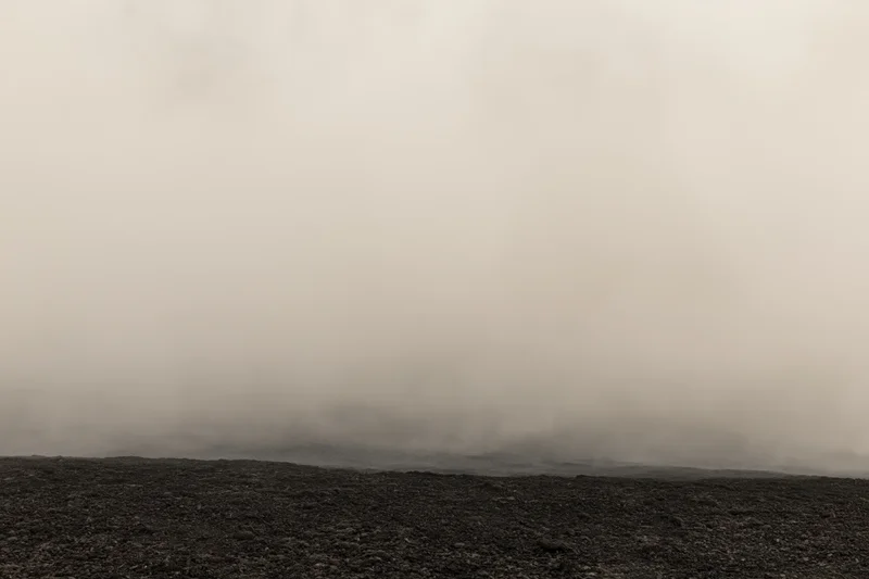 Thick smoke rolling low over dark rocky ground