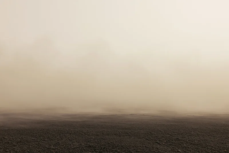 Thick dust cloud rolling low over dark rocky ground