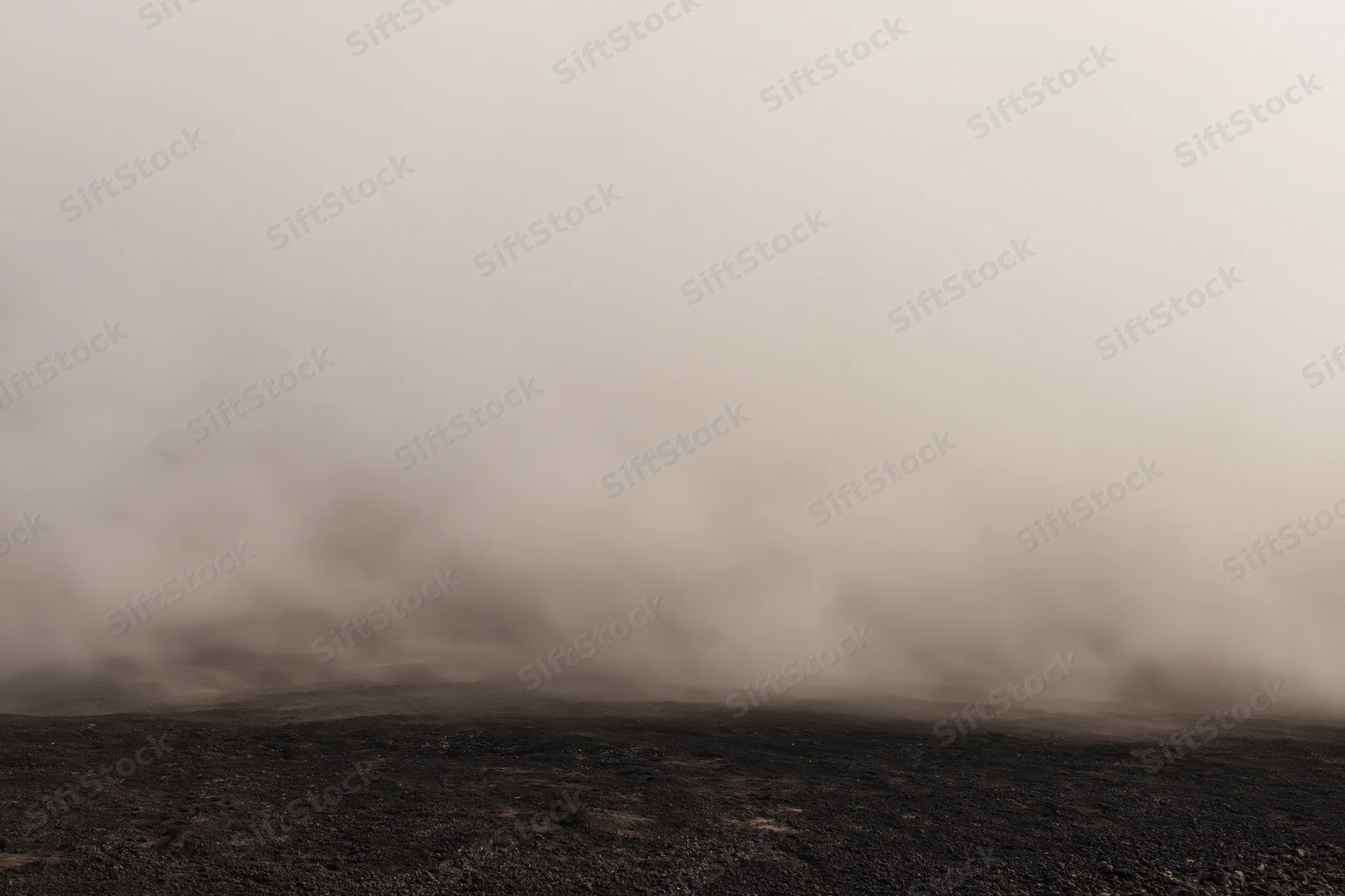 Thick smoke rolling low over dark rocky ground