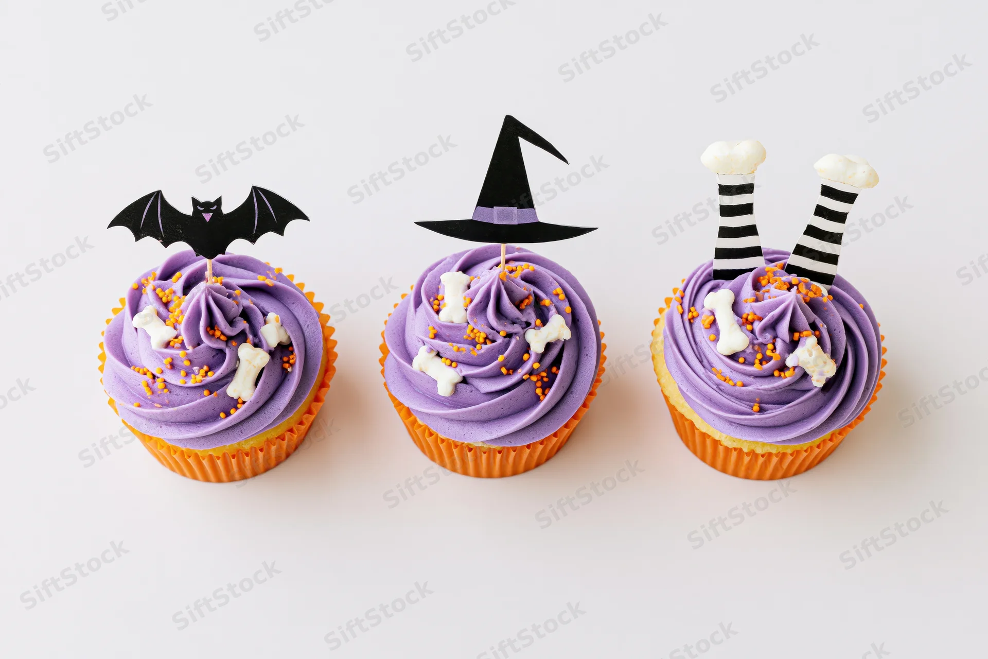 Three halloween-themed cupcakes with purple frosting and decorative toppers arranged in a row on a plain white surface