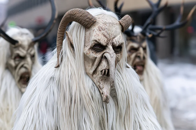 Krampus performers in traditional costumes with horned masks and white fur during a winter festival procession