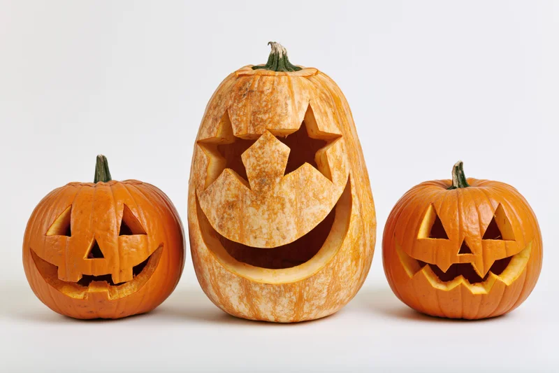 Three carved pumpkins arranged in a row on a white background