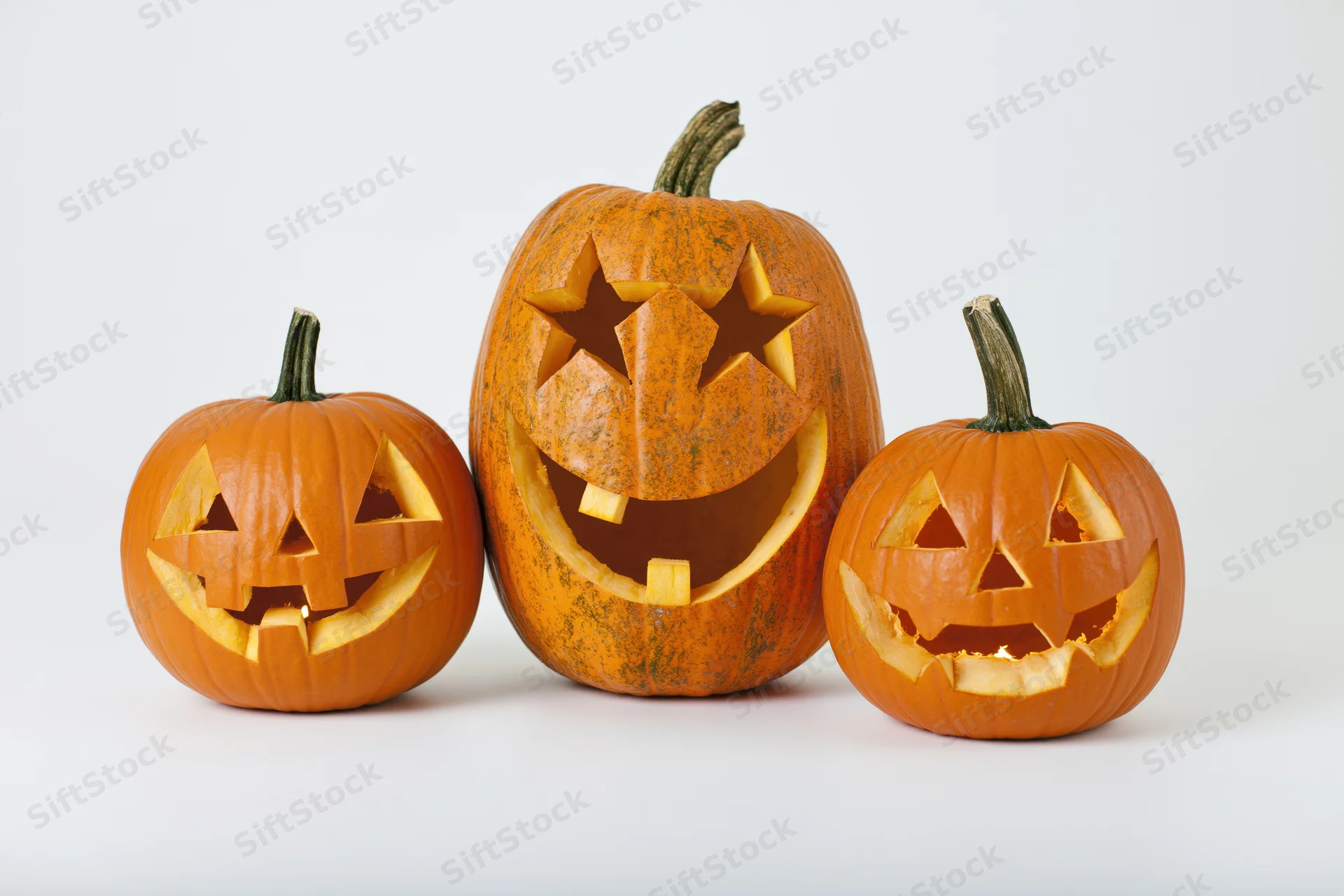 Three carved pumpkins arranged in a row on a white surface