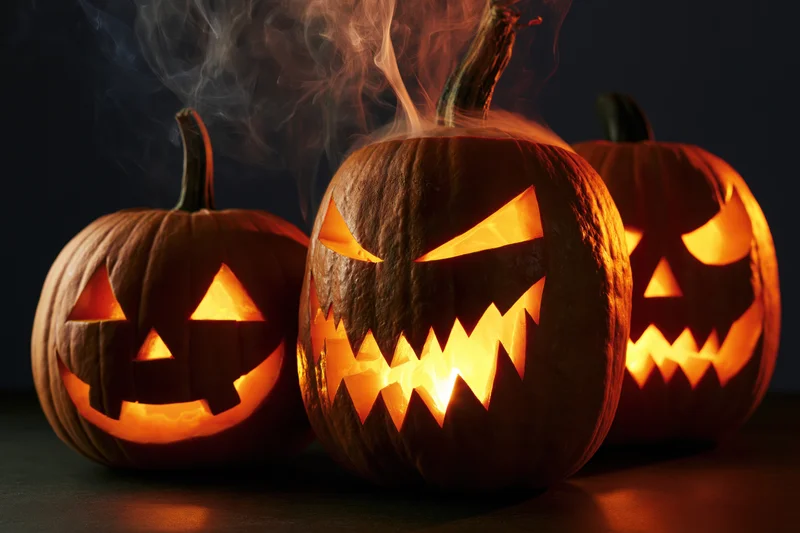 Three carved pumpkins glowing with smoke rising from them on a dark surface