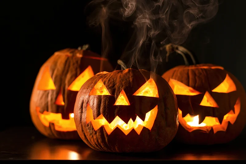 Three carved pumpkins glowing with smoke rising from them on a dark surface