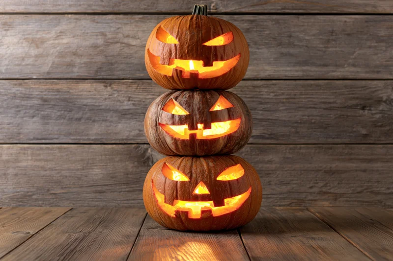 Three carved jack-o-lanterns stacked vertically on a wooden surface glowing with candlelight