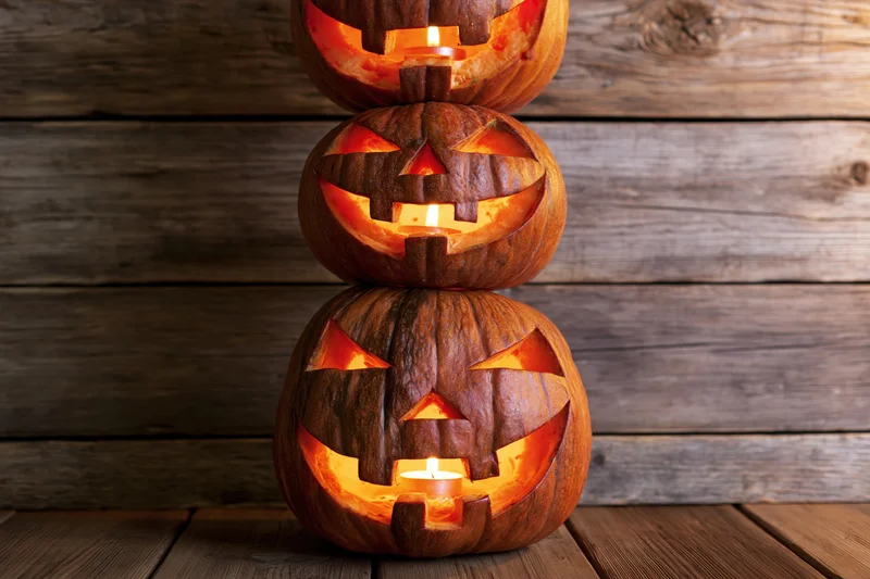 Three carved jack-o-lanterns stacked vertically on wooden surface with glowing candles inside