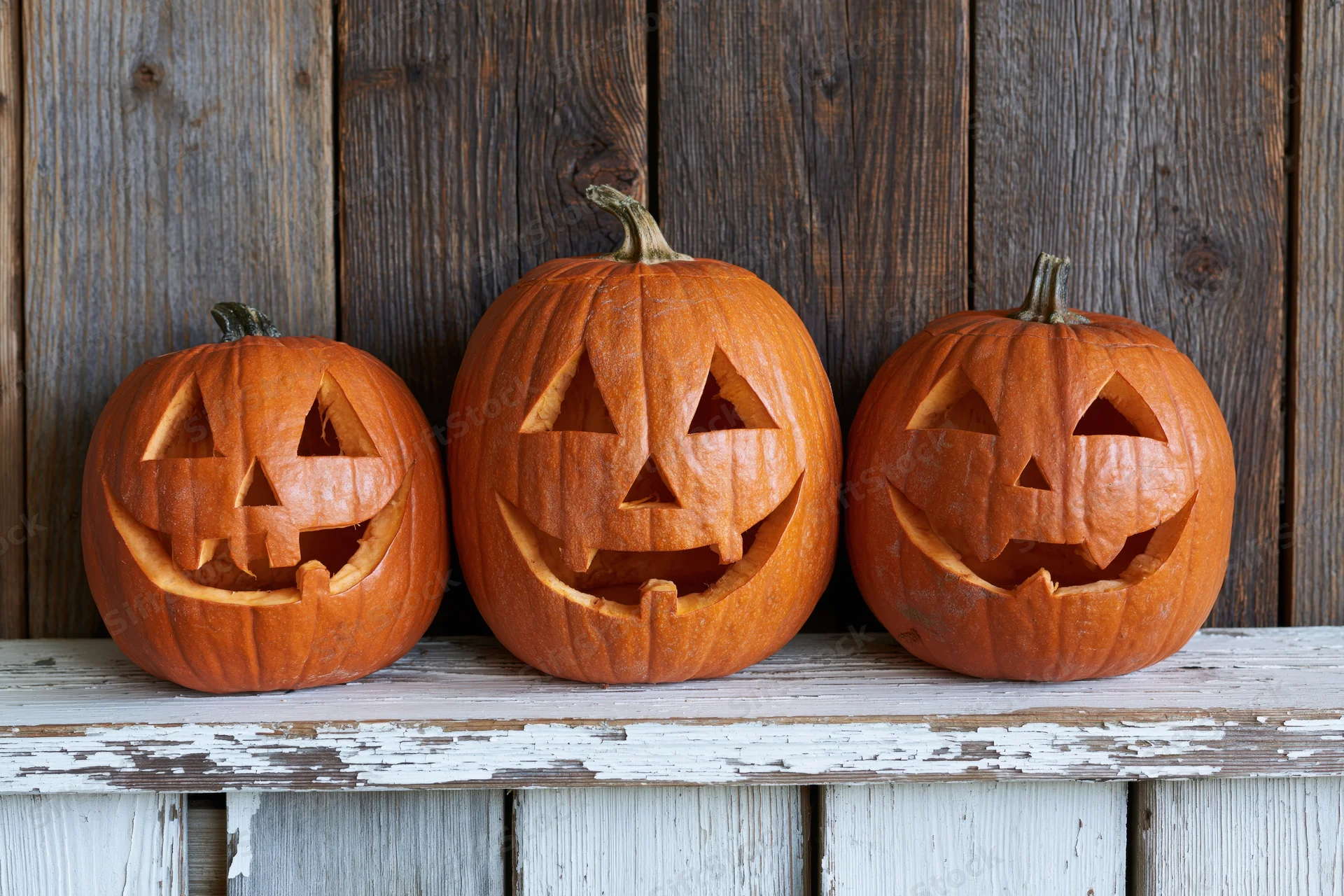 Three carved pumpkins with jack-o-lantern faces arranged on a weathered wooden shelf
