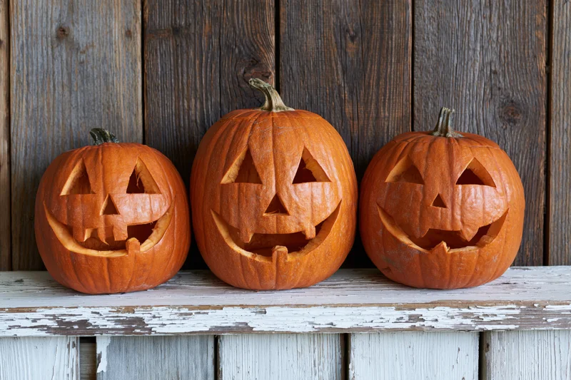 Three carved pumpkins with jack-o-lantern faces arranged on a weathered wooden shelf