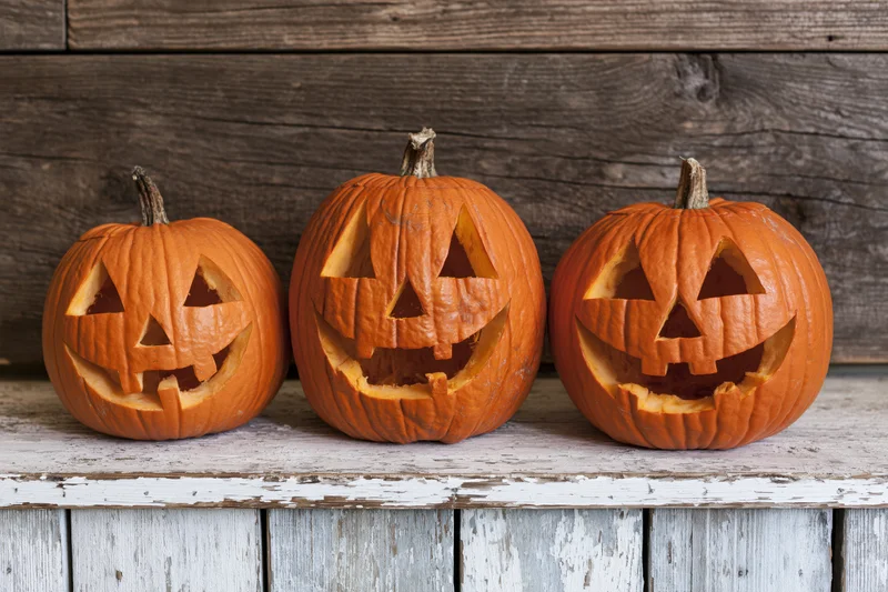 Three carved jack-o-lanterns arranged in a row on a weathered white wooden shelf against a dark wood background
