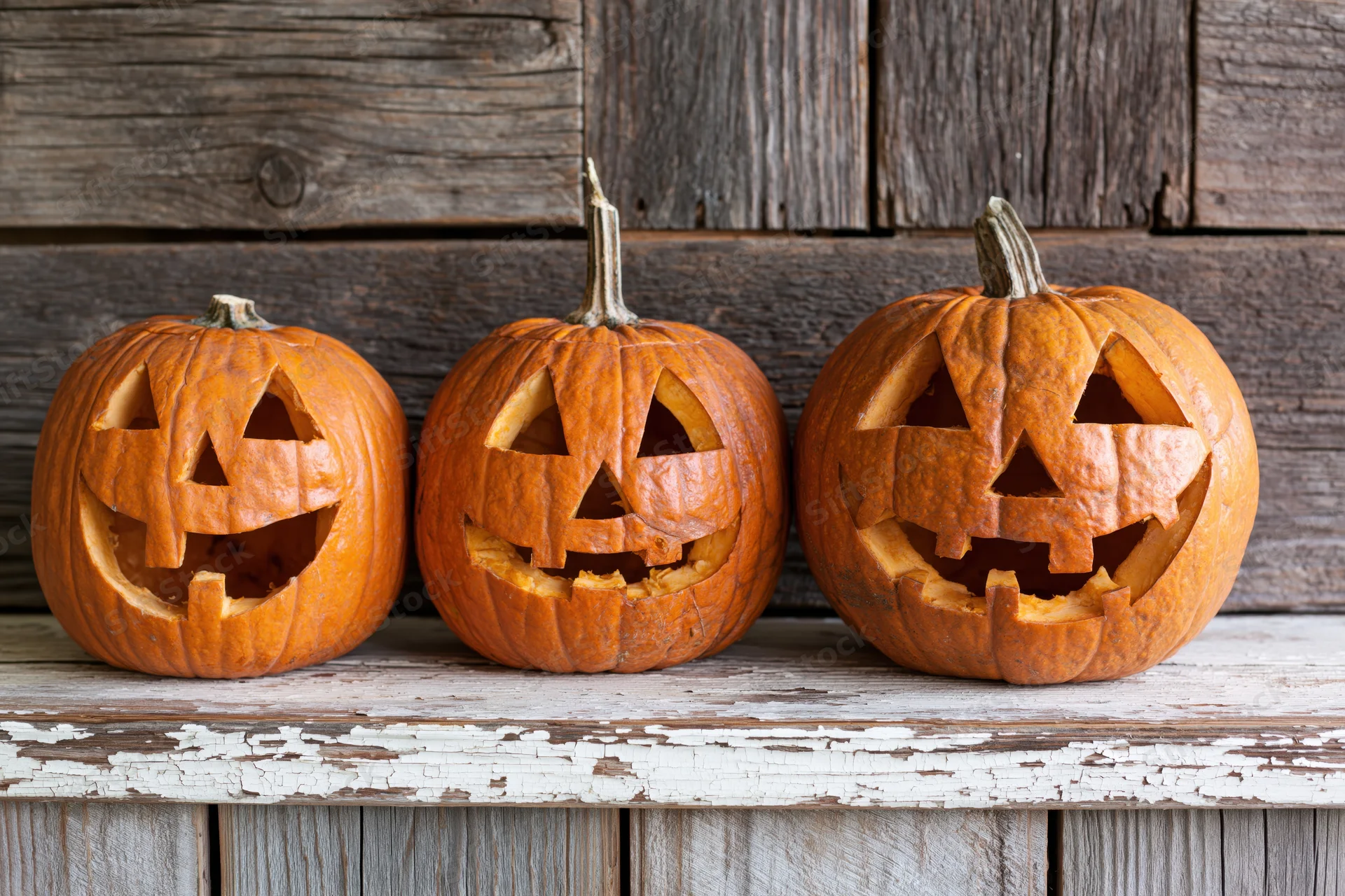 Three carved jack-o-lanterns with smiling faces arranged on a weathered wooden shelf