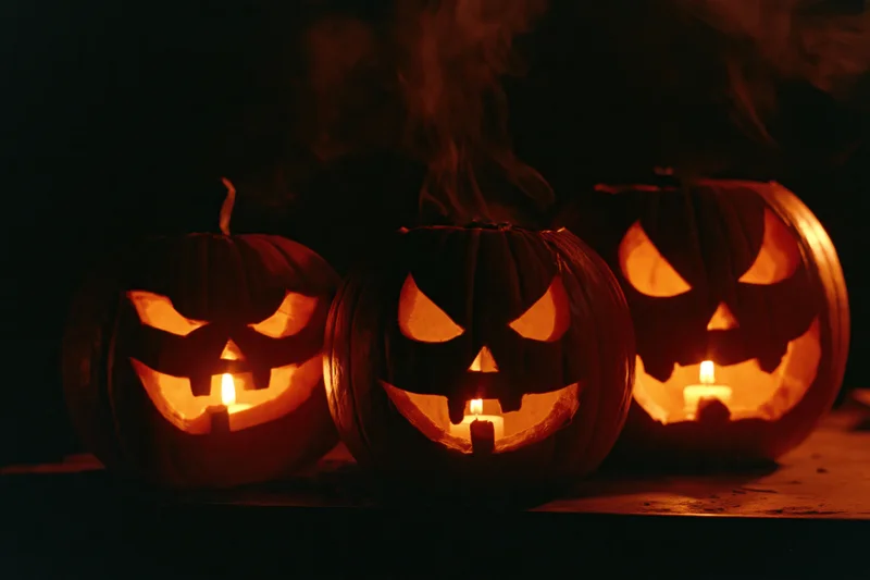 Three carved jack-o-lanterns glowing with candles on a dark surface at night
