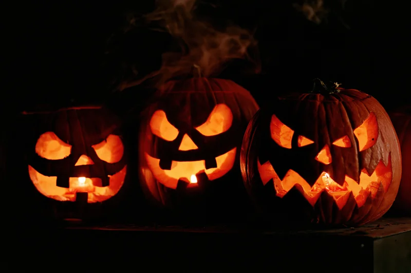 Three carved jack-o-lanterns glowing with candles in the dark