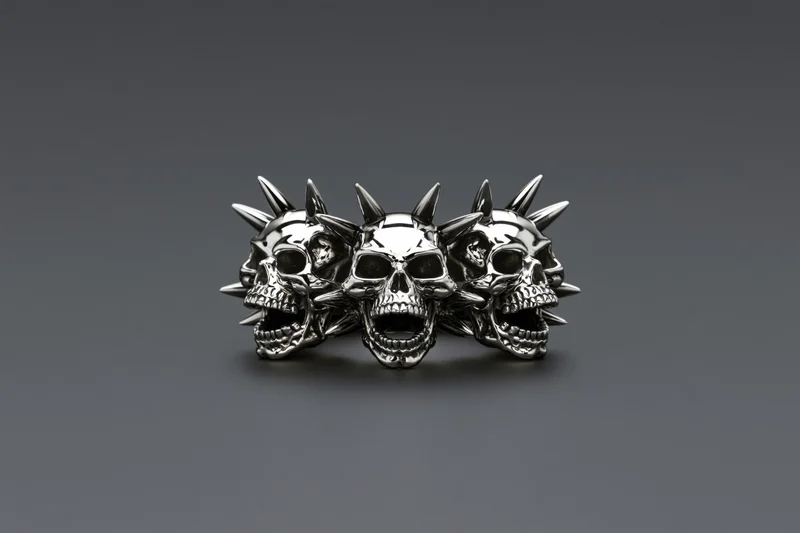 Three chrome skulls with open jaws and spikes arranged as a ring on a gray background