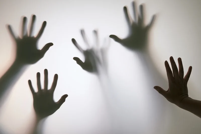Silhouetted hands pressing against frosted glass with soft light behind