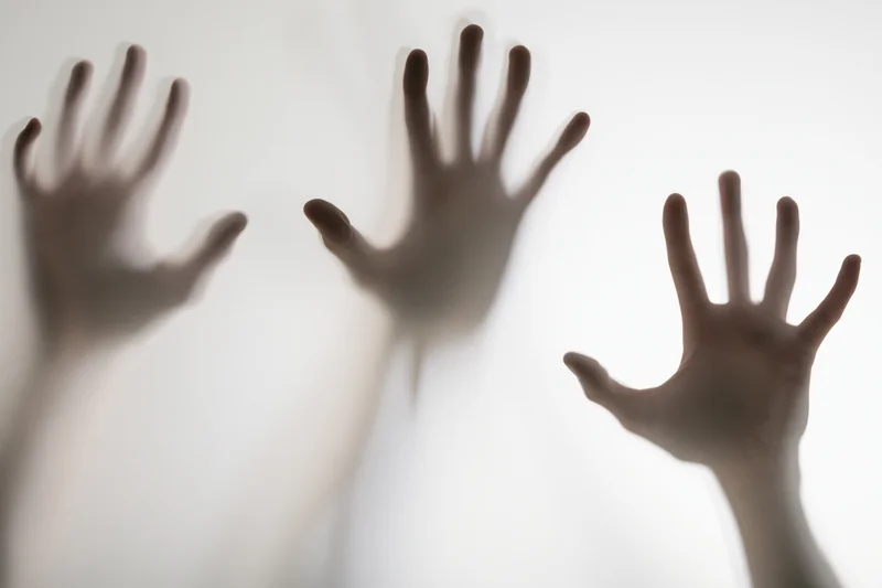 Three human hands pressing against frosted glass with blurred shadows and soft light diffusion