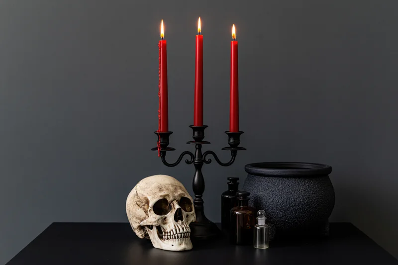 Skull and lit red candles in a black candelabra beside a cauldron and potion bottles on a dark table