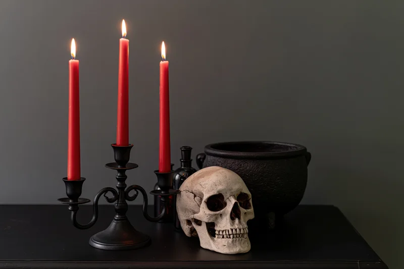 Skull and lit red candles in a black iron candelabra beside a cauldron on a dark table