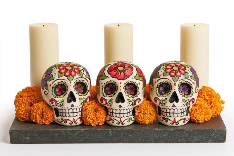 Three painted sugar skulls arranged on a dark stone altar with marigolds and candles