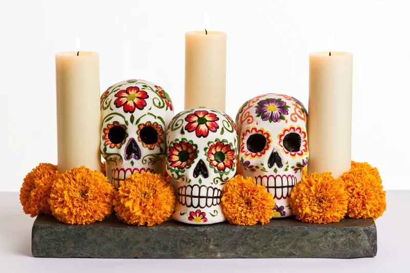 Three painted sugar skulls arranged on a stone base with candles and marigolds for day of the dead celebration