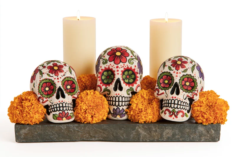 Three painted sugar skulls arranged on a stone base with candles and marigolds for day of the dead celebration