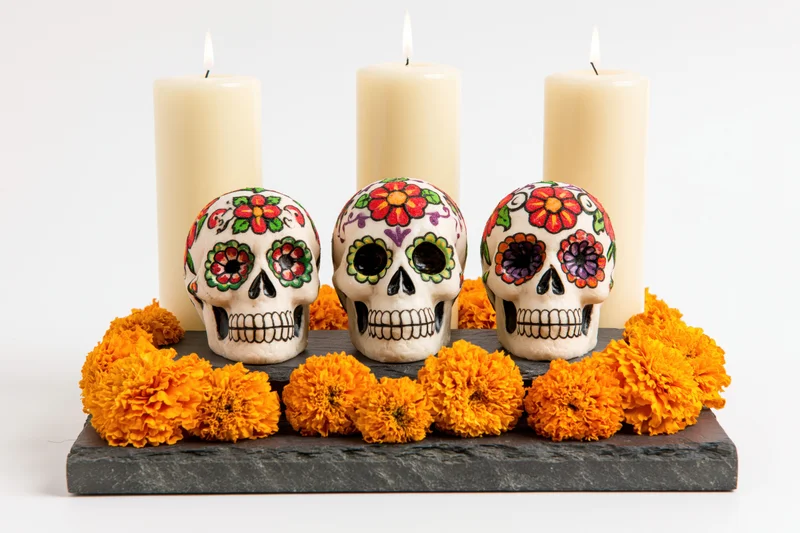 Three painted sugar skulls on a stone altar with marigolds and candles