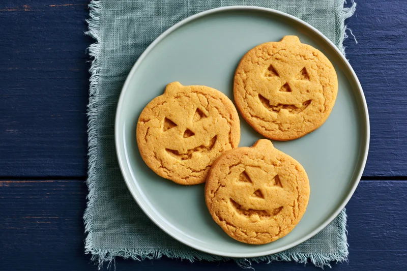 Three jack-o-lantern sugar cookies on a plate set on a cloth napkin over a wooden table