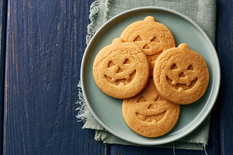 Round jack-o-lantern sugar cookies on a plate set on a dark wooden table with a cloth napkin