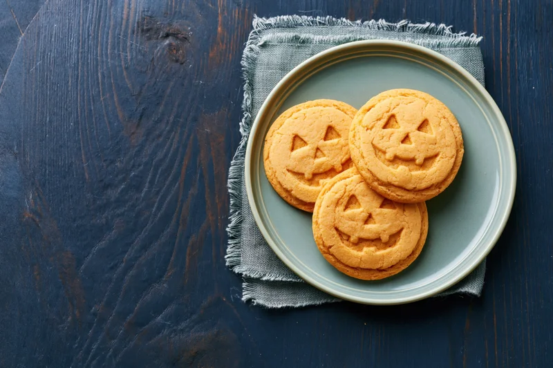 Three jack-o-lantern sugar cookies on a plate resting on a cloth napkin on a dark wooden table