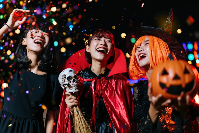 Three young asian women in halloween costumes laughing with confetti and decorations at night