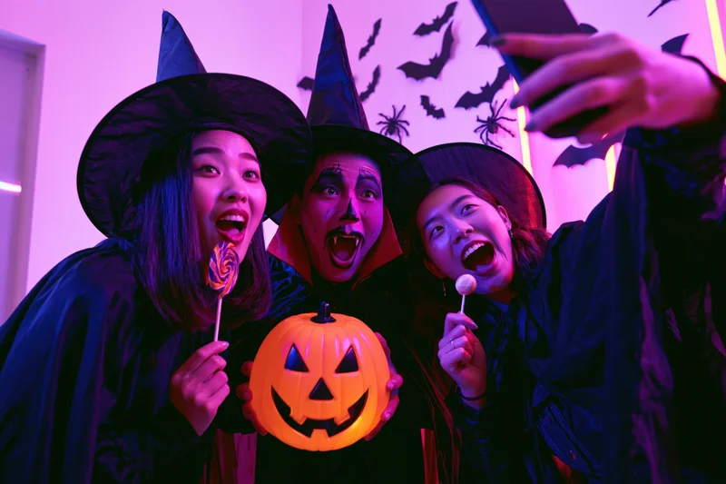 Three young asian adults in halloween costumes taking a selfie indoors with pumpkin and candy