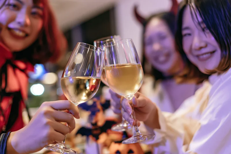 Three young asian women in halloween costumes clinking wine glasses at a party
