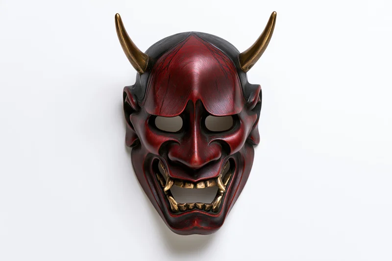 Traditional japanese hannya noh theater mask with red face black horns and gold teeth displayed on white background