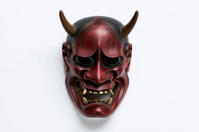 Traditional japanese hannya noh theater mask with red face black horns and gold teeth on white background