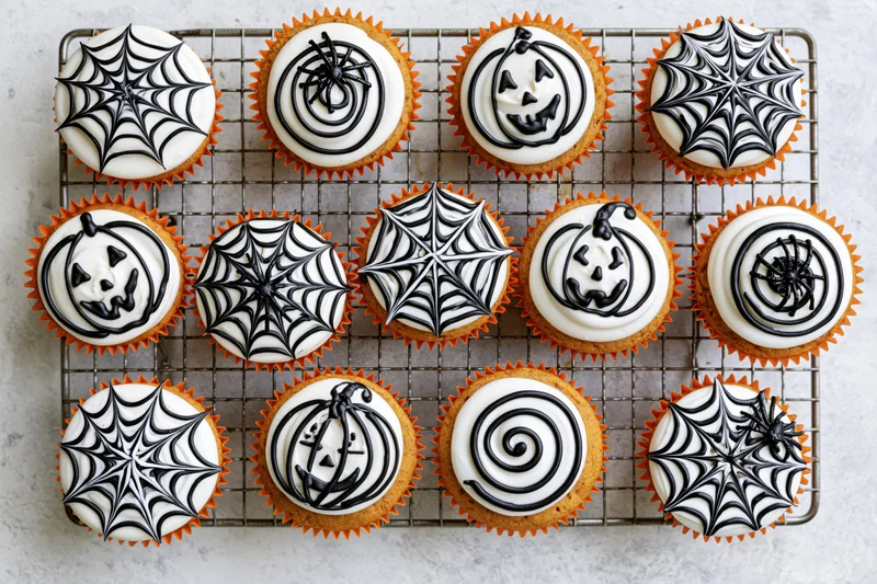 Twelve halloween cupcakes with spiderweb and jack-o-lantern frosting on a wire rack