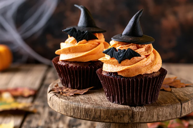 Two halloween cupcakes with orange frosting and witch hats on a wooden platter